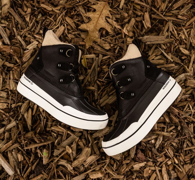 a pair of black and white Wolverine boots on wood chips