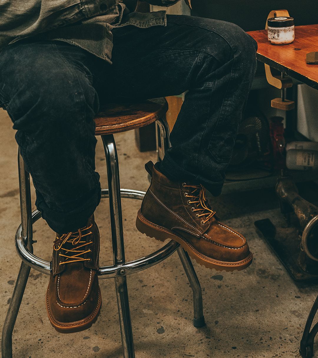 Sitting on a shop stool wearing dark jeans and tan Floorhand boots.