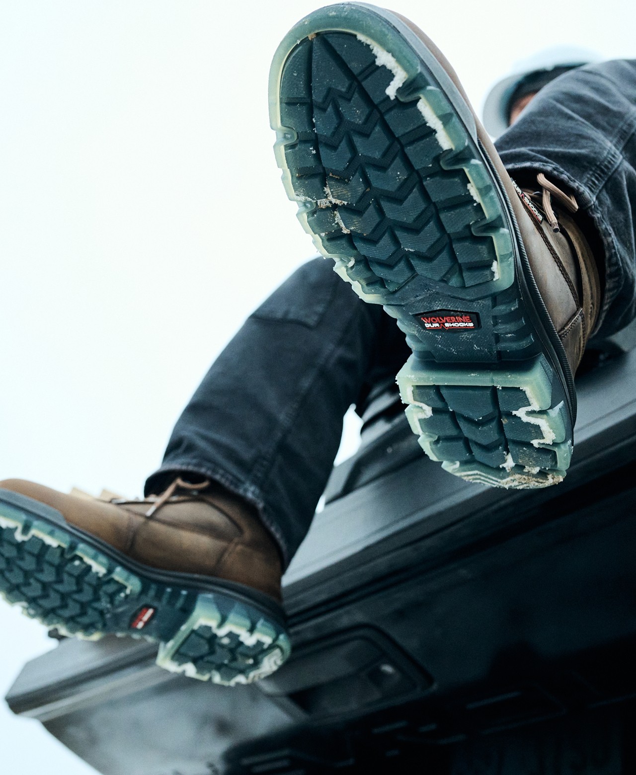 Work boot soles raised up against a bright winter sky.