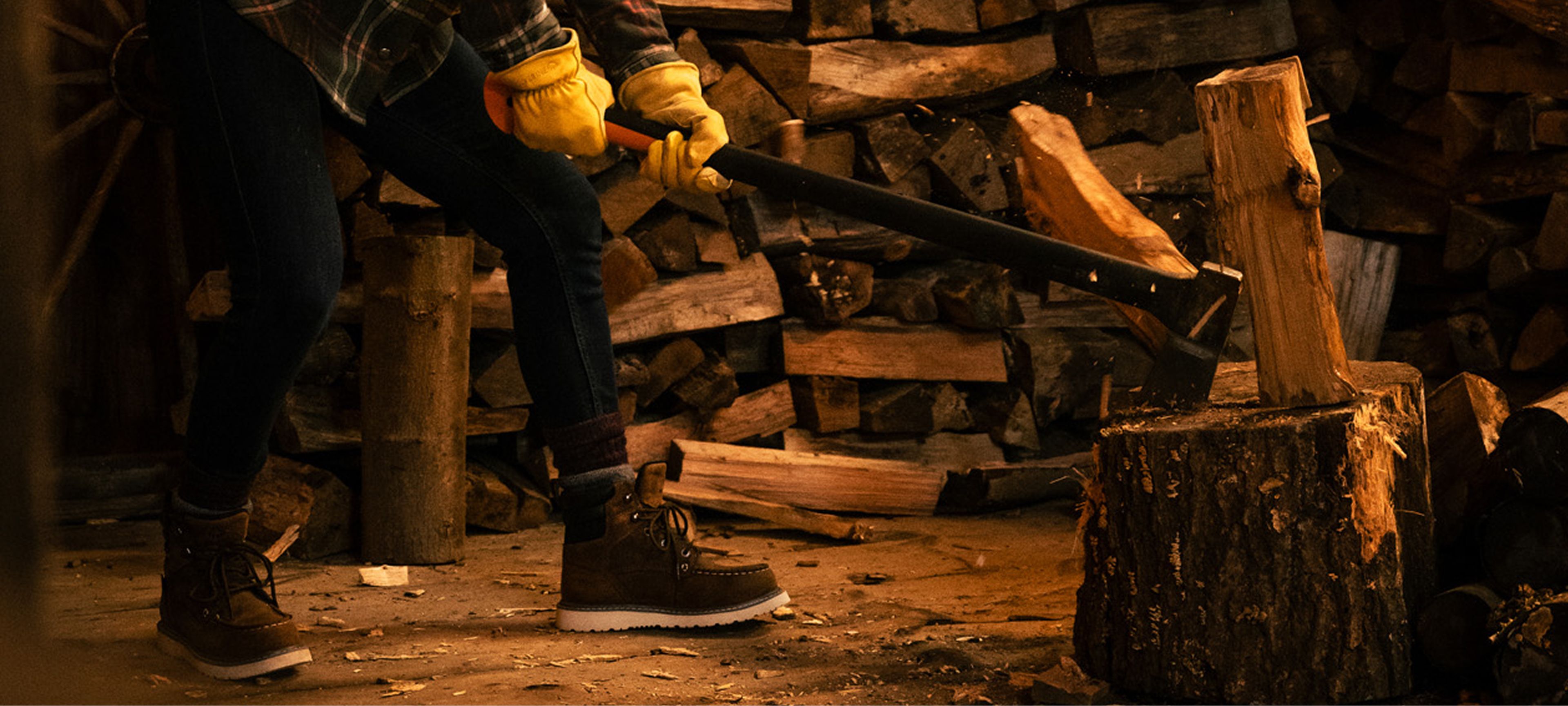 Splitting wood with an axe, wearing jeans, boots, gloves, and a warm Wolverine jacket.