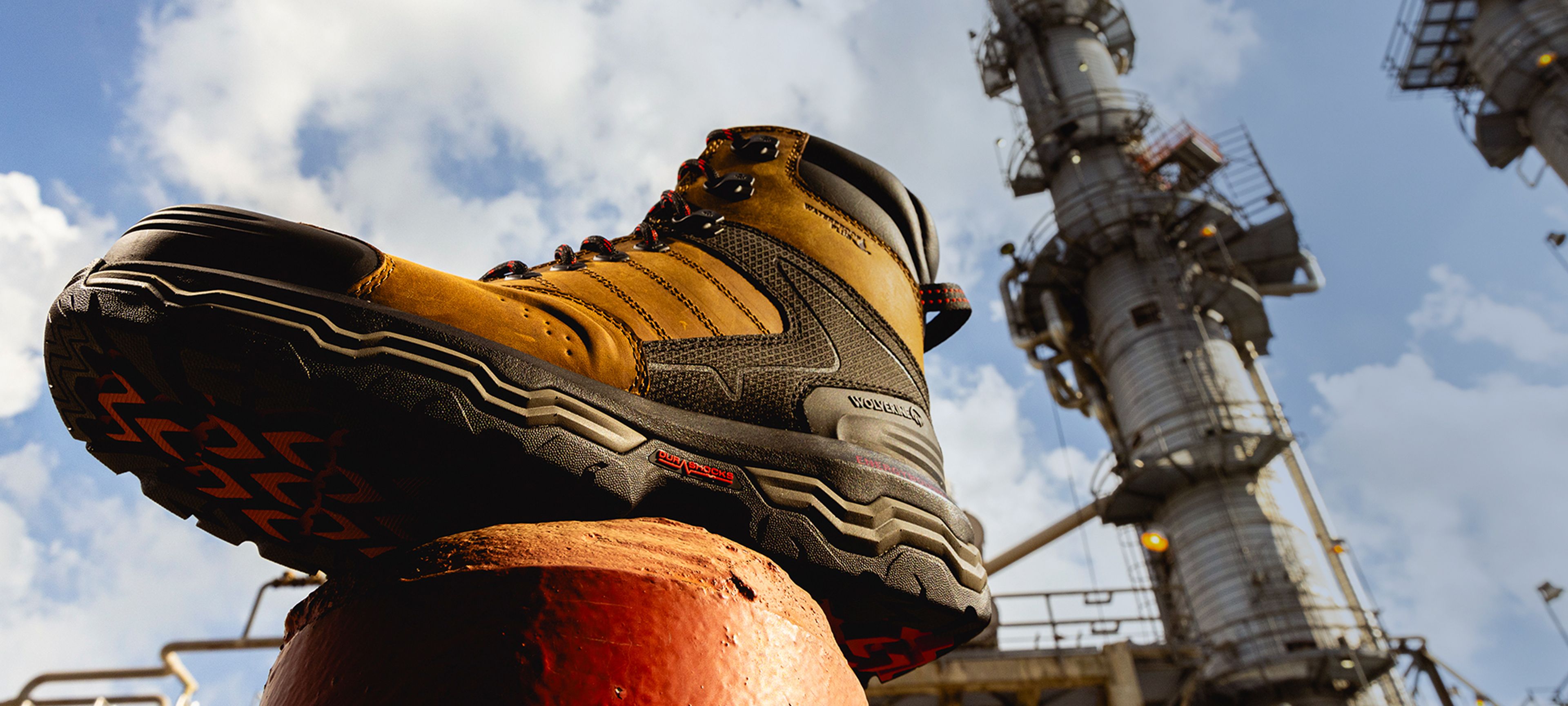 Boot on a steel and concrete post in front of a factory chimney.