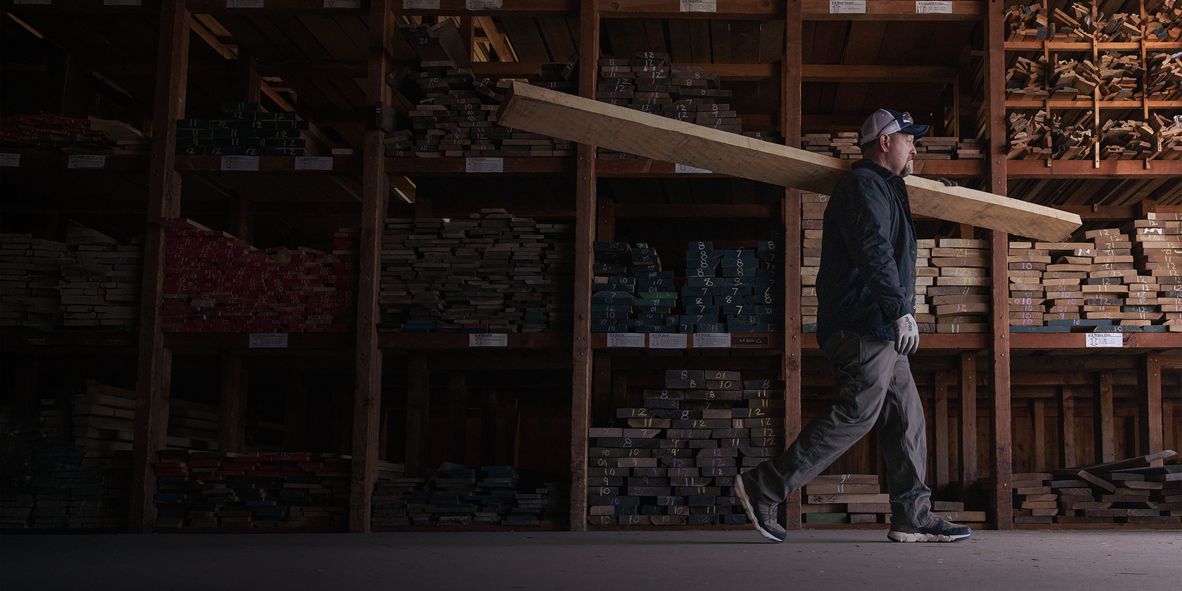 Carrying a rough-sawn board past racks of dimensional lumber.