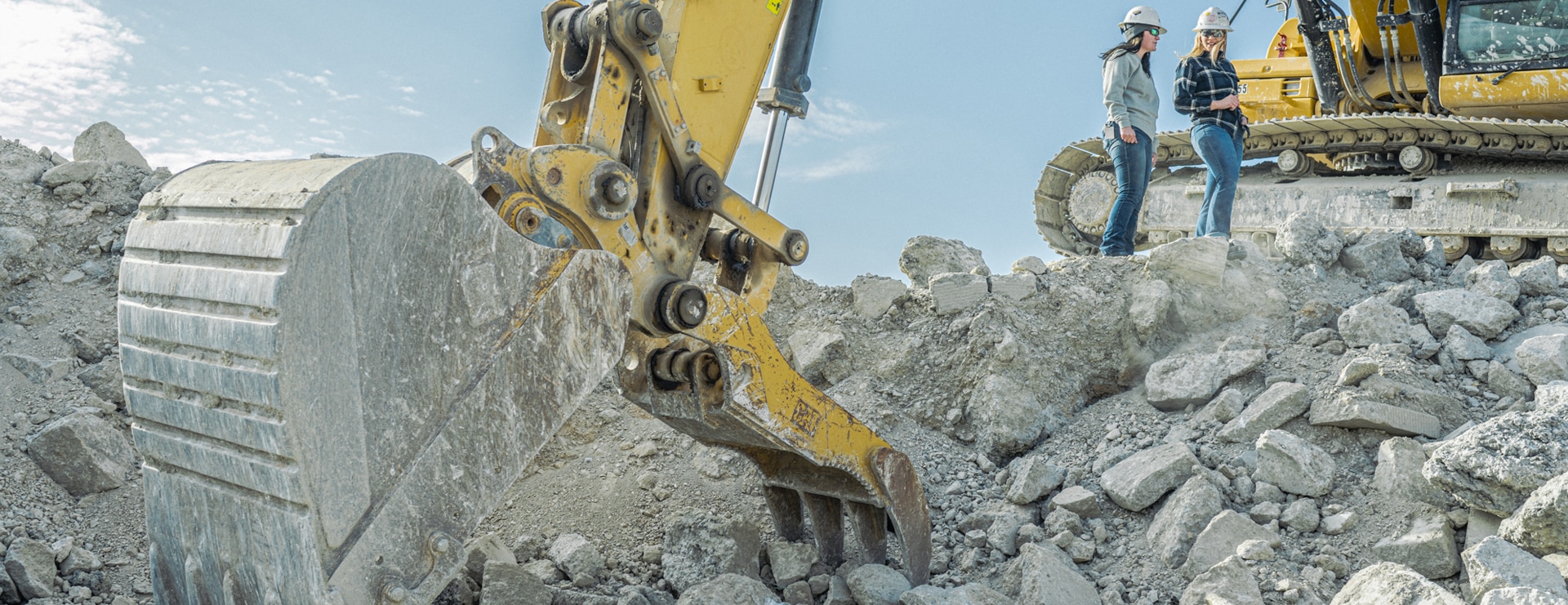 Construction crane digging in a pile of rubble with two workers in the background.