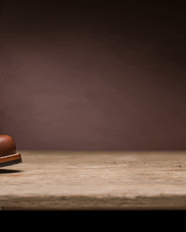 A brown leather boot on a hard wooden surface with a brown background.