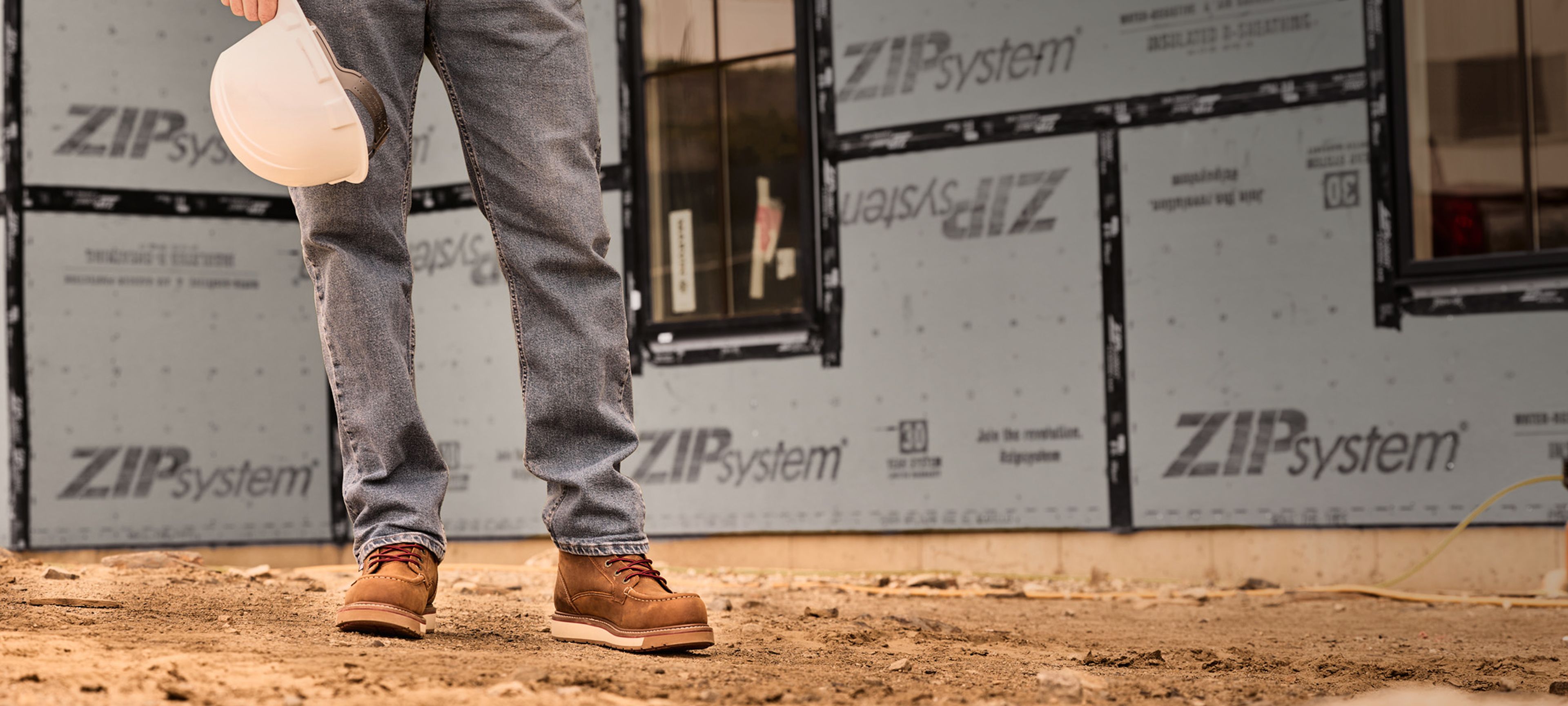 Worker's legs standing in front of a modern building under construction wearing USA-Built boots.