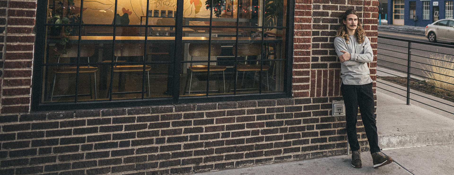 Caleb leaning against the outside brick wall of a coffee shop.
