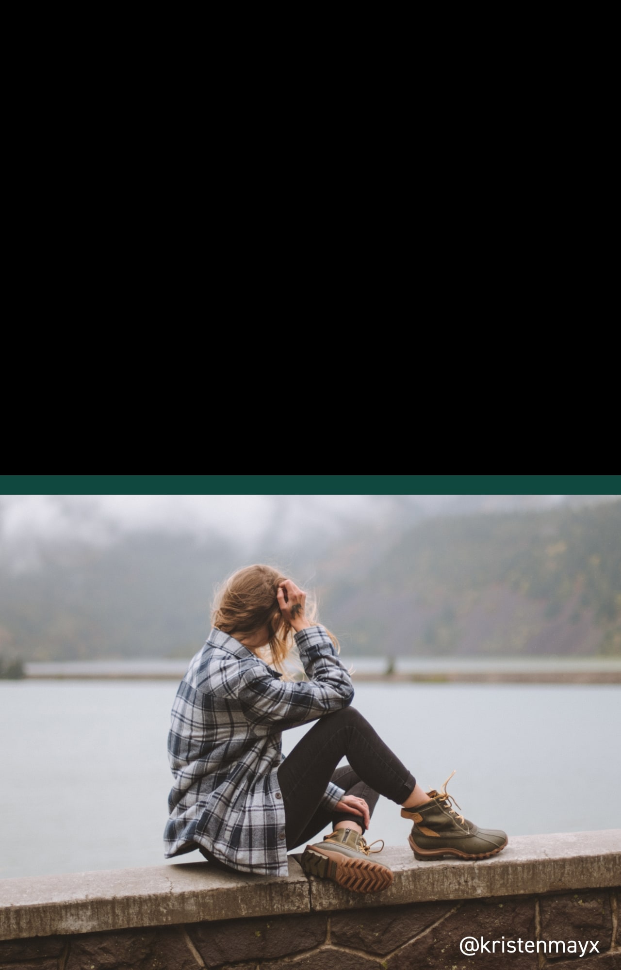 Person wearing Torrent boots sitting on a ledge overlooking a lake.