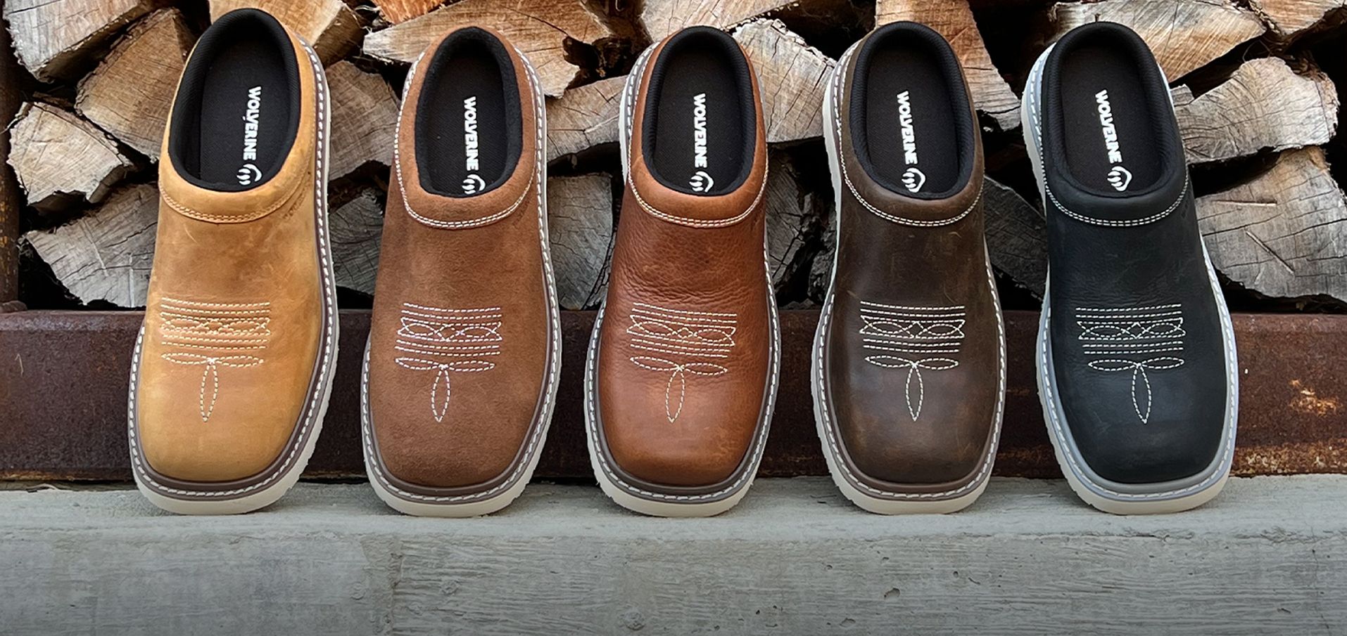 Five colors of Bronc Clog slip-on shoes leaning against a woodpile.
