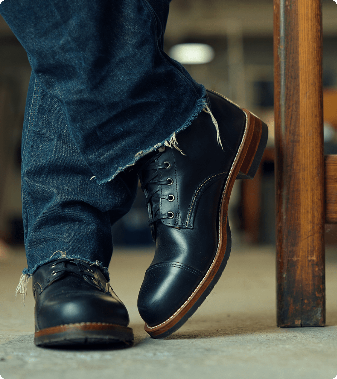 Standing with legs crossed wearing dark jeans and black boots.