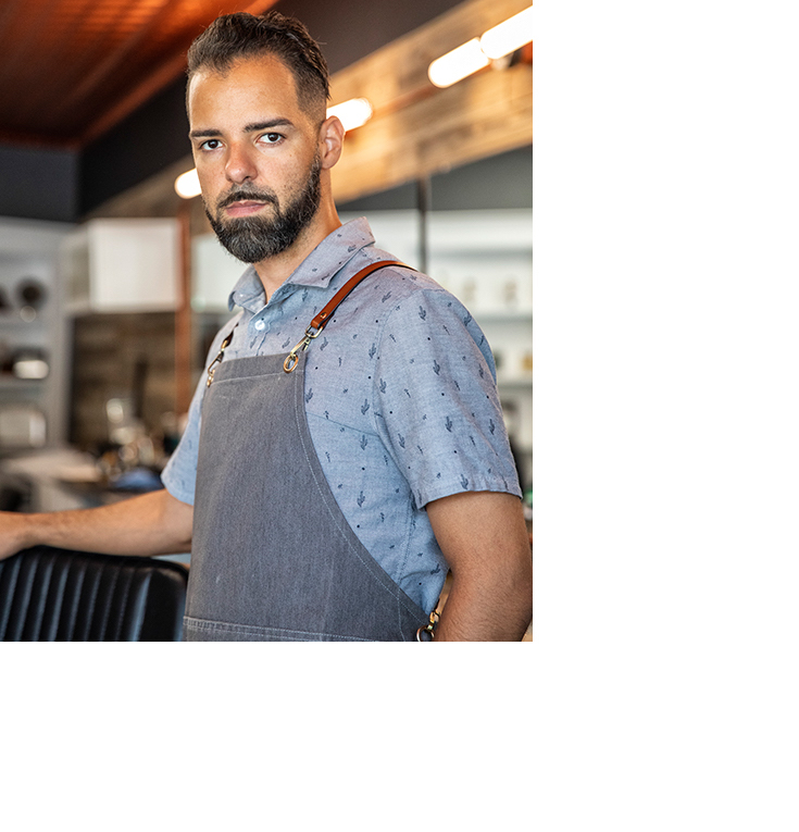 Headshot of Tommy R. wearing a barber's apron.