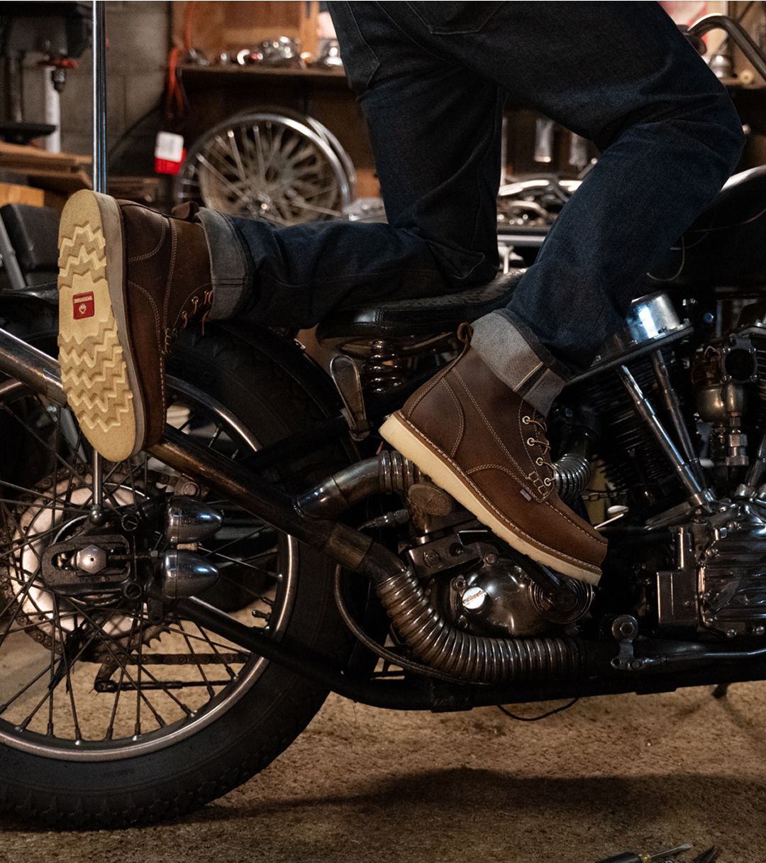 Kneeling on the seat of a motorbike wearing dark jeans and brown Workshop Wedge boots.
