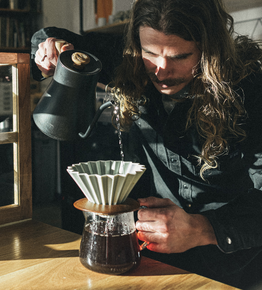 Caleb carefully pouring coffee through a filter.