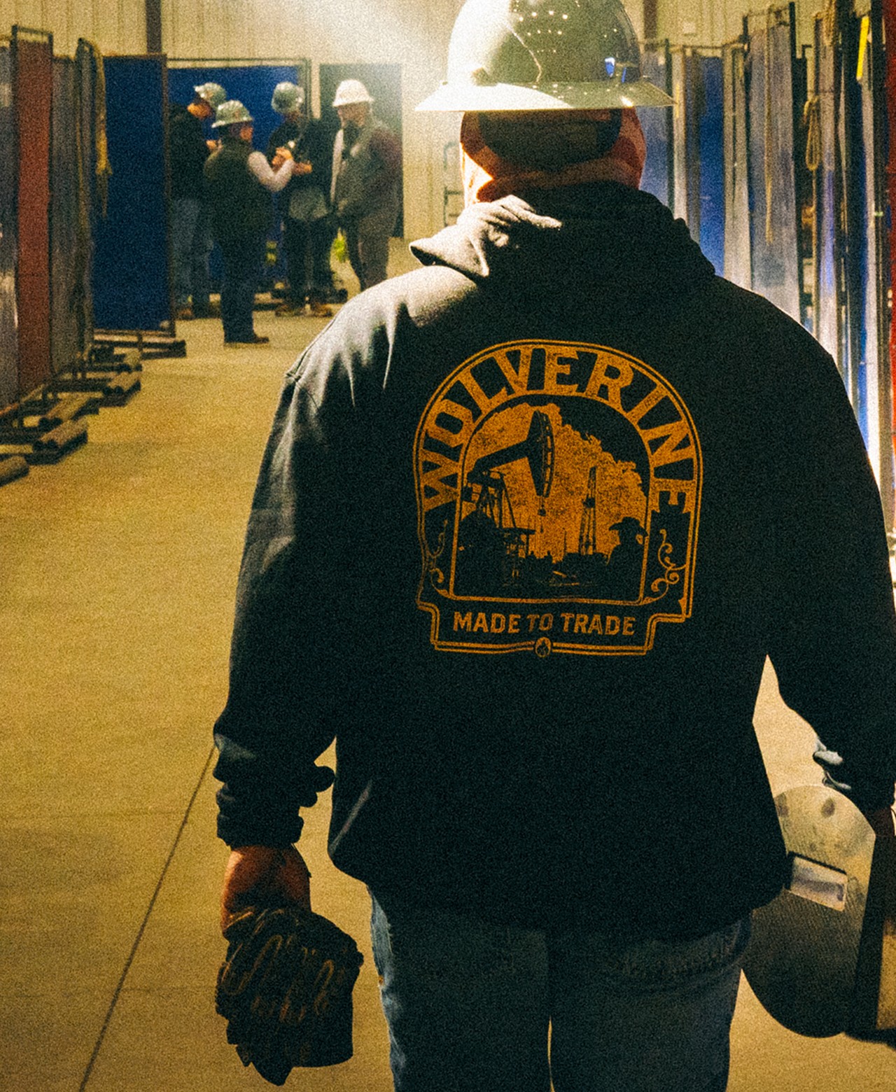 A worker in a hard hat and Wolverine hoodie walking through a warehouse.