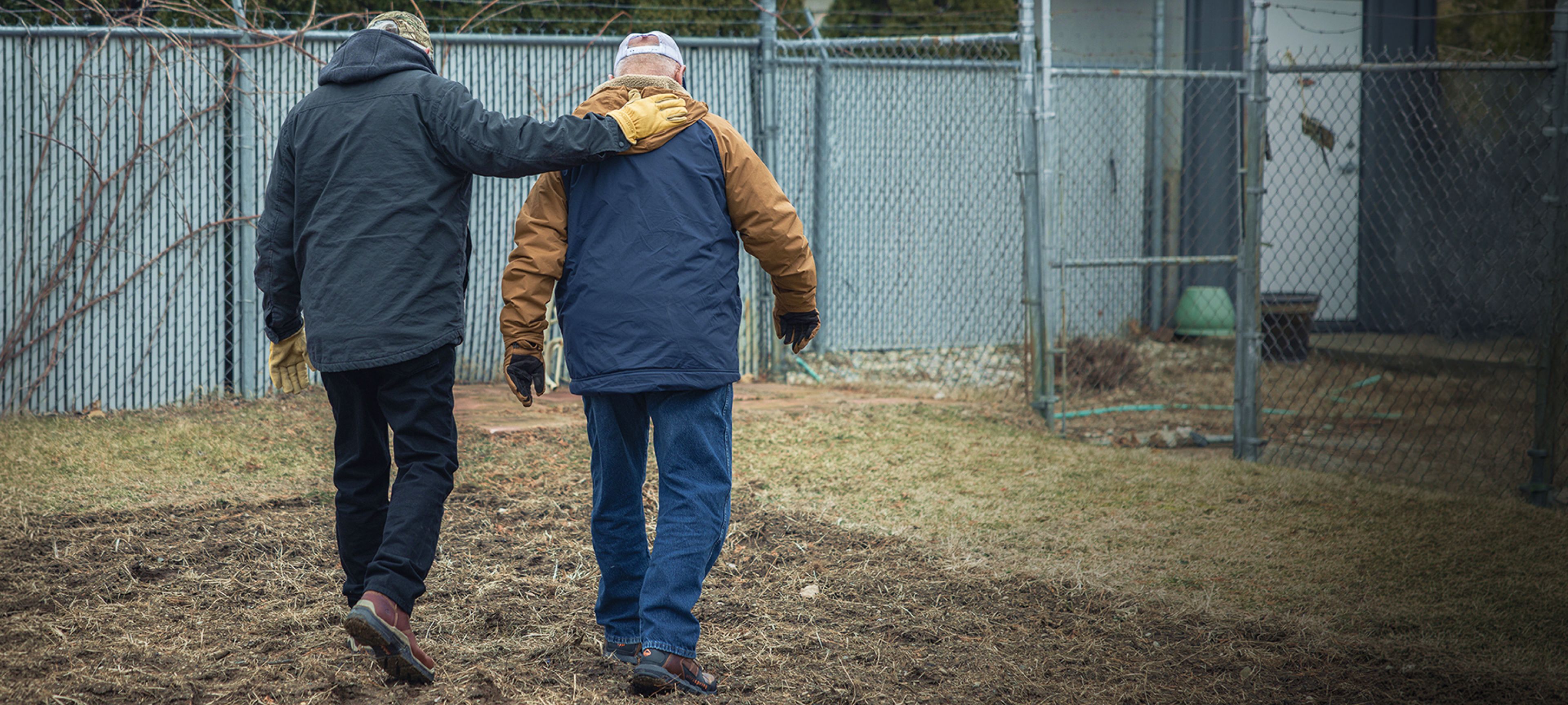 Adult son with arm around father walking away together.